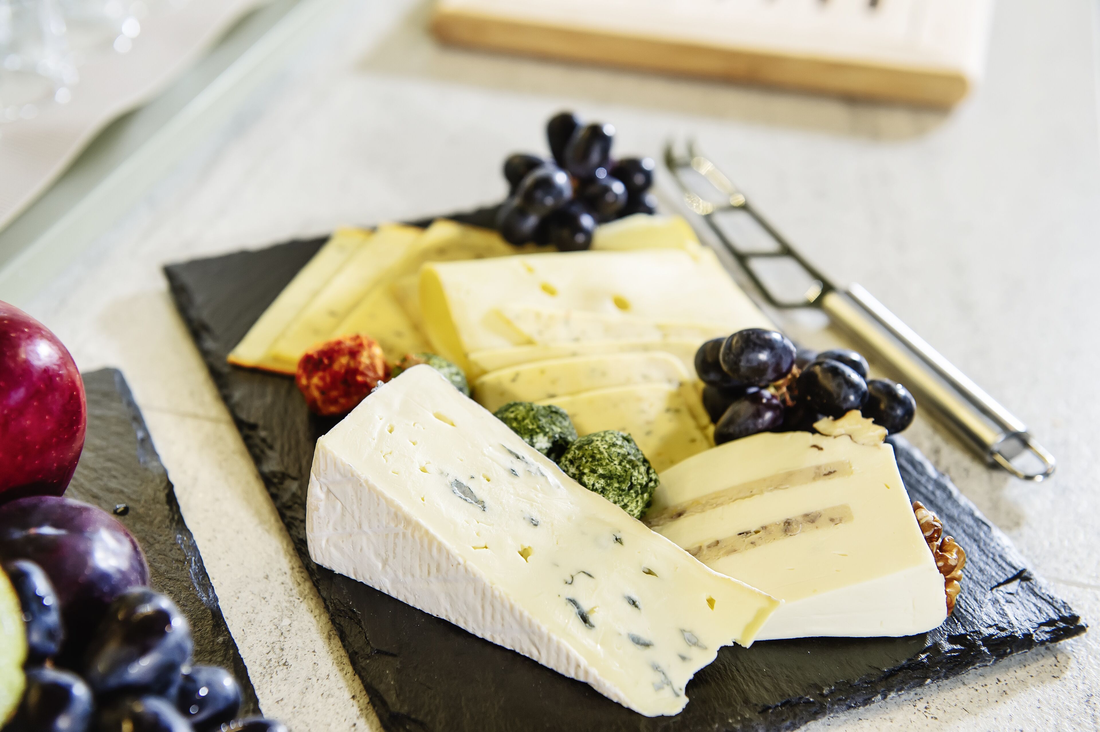 Una selección de quesos y frutas sobre una tabla de pizarra.