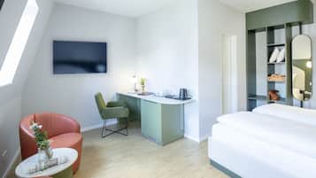 Ein modernes Hotelzimmer mit einem Bett, einem Schreibtisch mit Stuhl, einem an der Wand befestigten Fernseher und einem kleinen Tisch mit einer Vase.