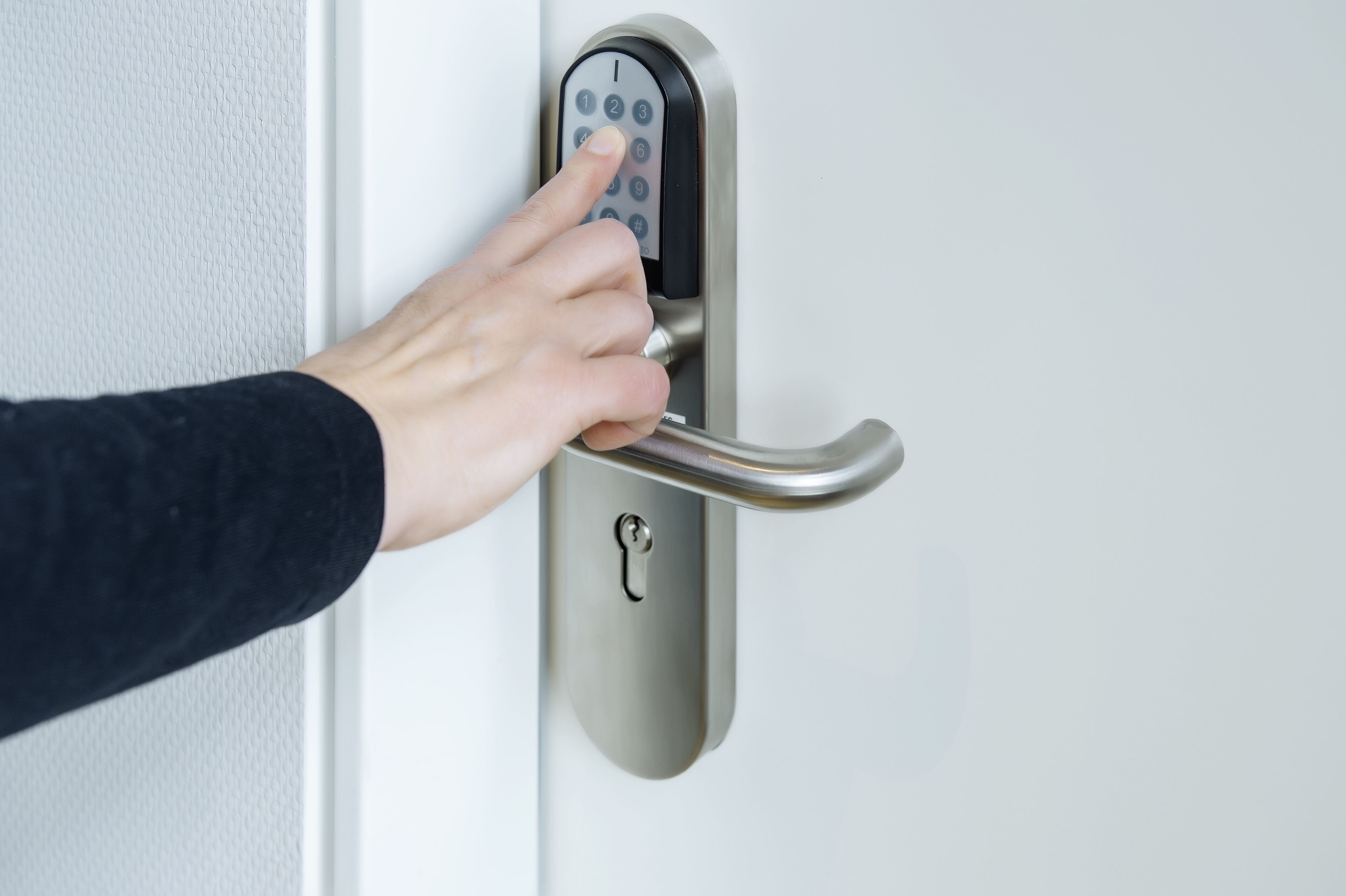 A hand using a numeric keypad on a modern door lock.