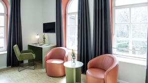 Una habitación moderna con escritorio, dos sillas, una mesita con un florero y ventanas grandes con cortinas.