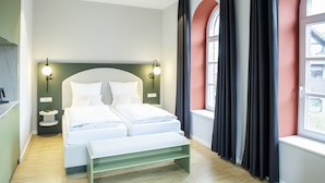 Una habitación de hotel moderna con una cama grande, dos mesitas de noche, un banco y una ventana con cortinas.