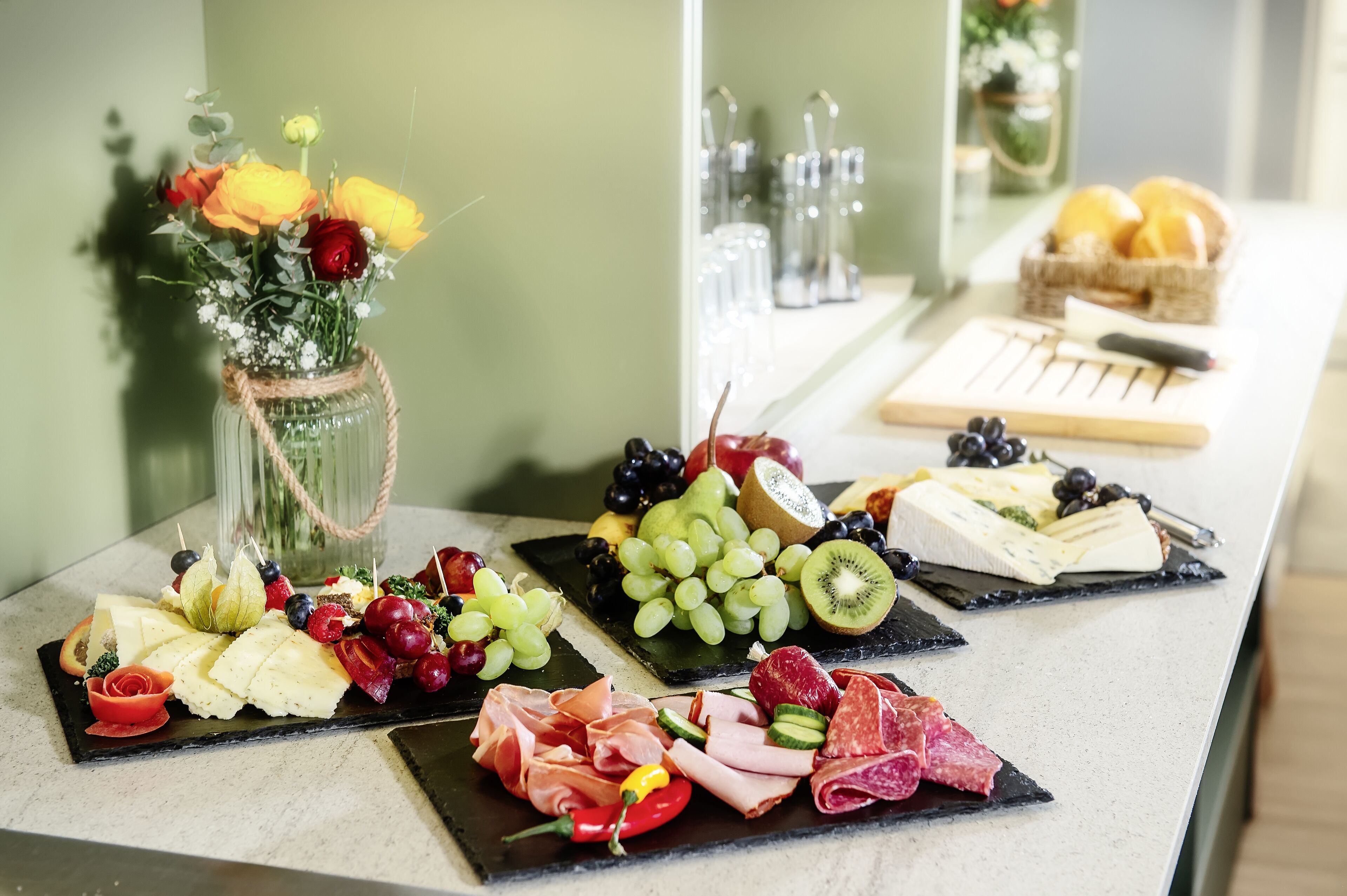 Eine Auswahl an Käse, Obst und Fleisch, ansprechend auf einer Theke drapiert.