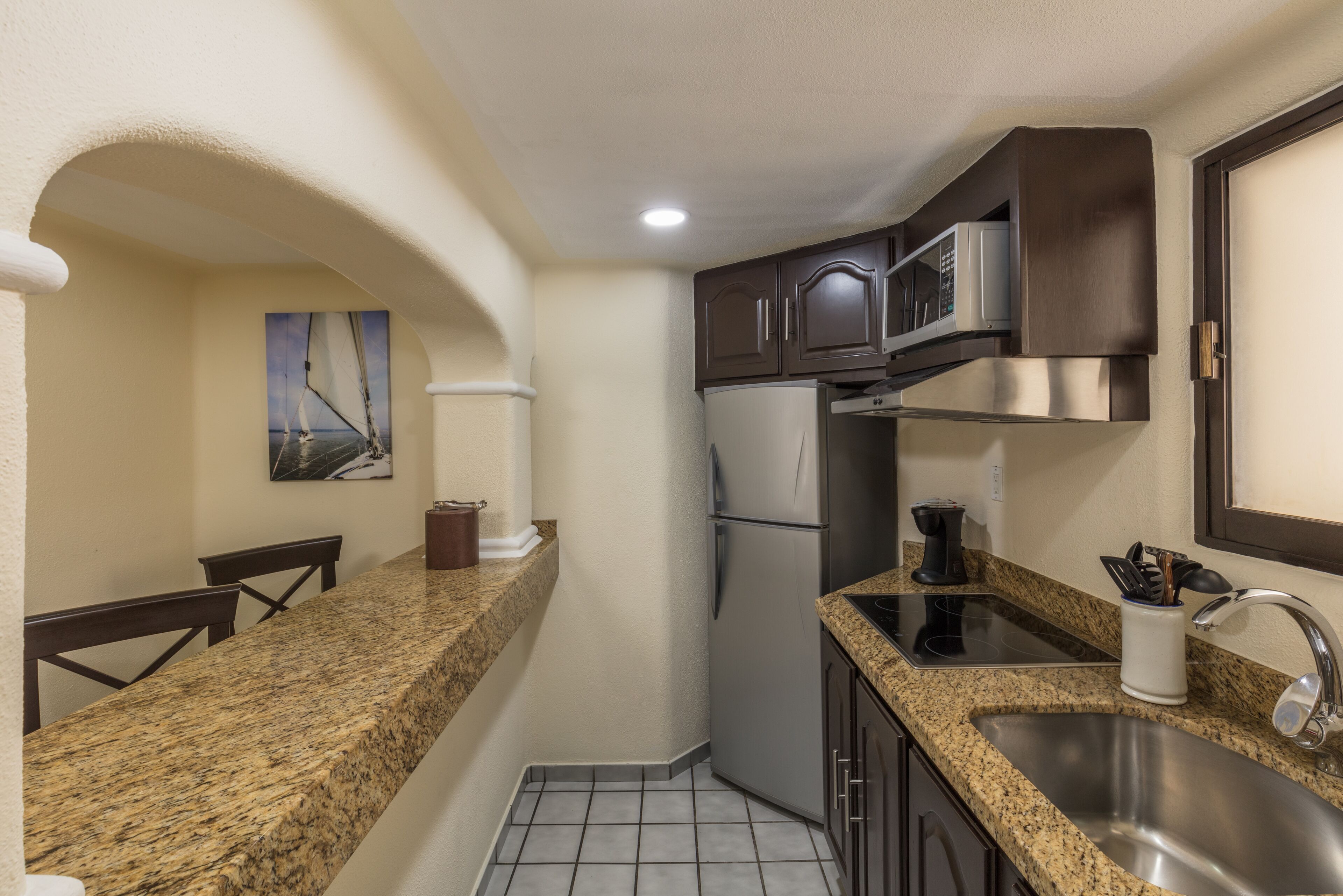 A compact kitchen with granite countertops, a stainless steel sink, a microwave, and a refrigerator.