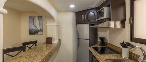 A compact kitchen with granite countertops, a stainless steel sink, a microwave, and a refrigerator.
