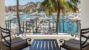 Un balcon avec deux chaises et une table, donnant sur une marina où sont amarrés des bateaux, avec une vue sur la ville en arrière-plan.