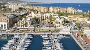 Un port de plaisance où sont amarrés de nombreux bateaux, entouré d’un paysage urbain côtier avec des bâtiments et une vue sur la mer.