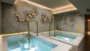 Un espace spa comprenant deux baignoires en marbre, un mur à texture et des œuvres d’art décoratives.
