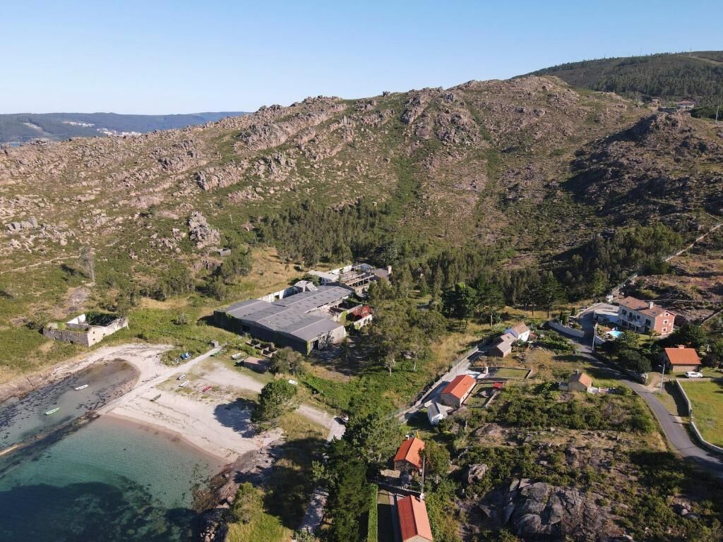 Ein Luftbild einer Küstenregion mit Strand, felsigem Gelände und verstreuten Gebäuden.
