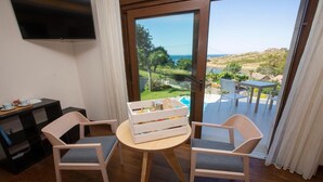 A room with a wooden table and two chairs, a TV mounted on the wall, and a view of a pool and landscape through a glass door. - A Ballenera de Caneliñas (Cee)