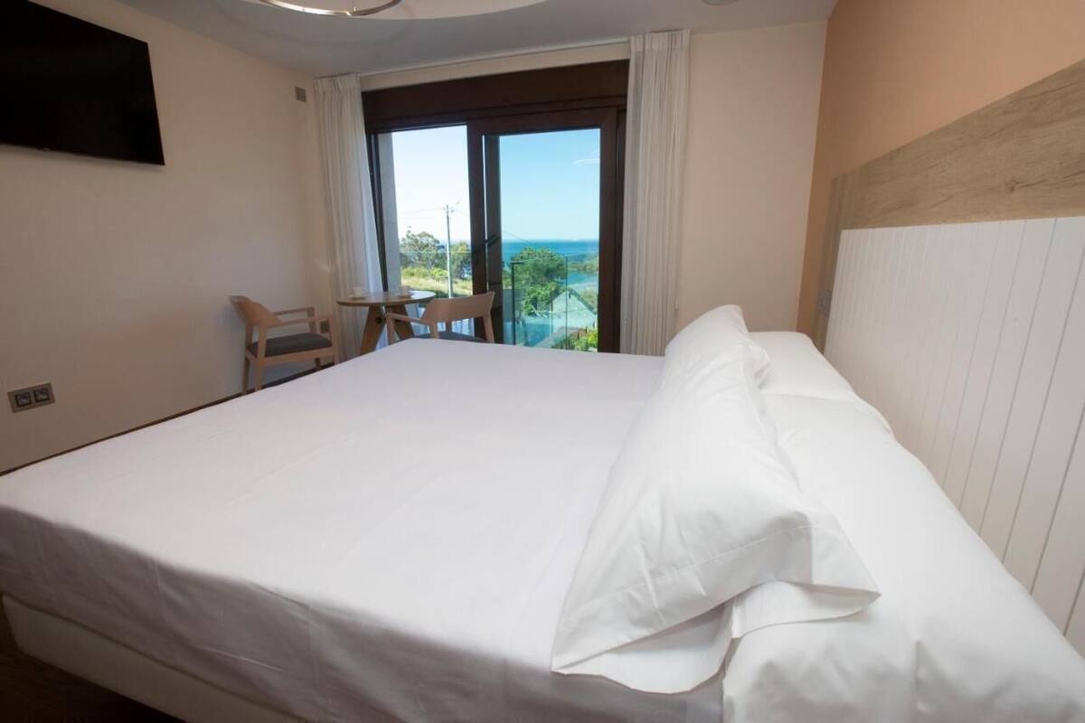 Une chambre d’hôtel avec un grand lit, un téléviseur fixé au mur, un balcon avec vue et une petite table avec des chaises.