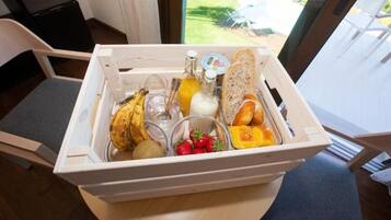 En træbakke med madvarer, herunder brød, bananer, yoghurt og jordbær på et bord.