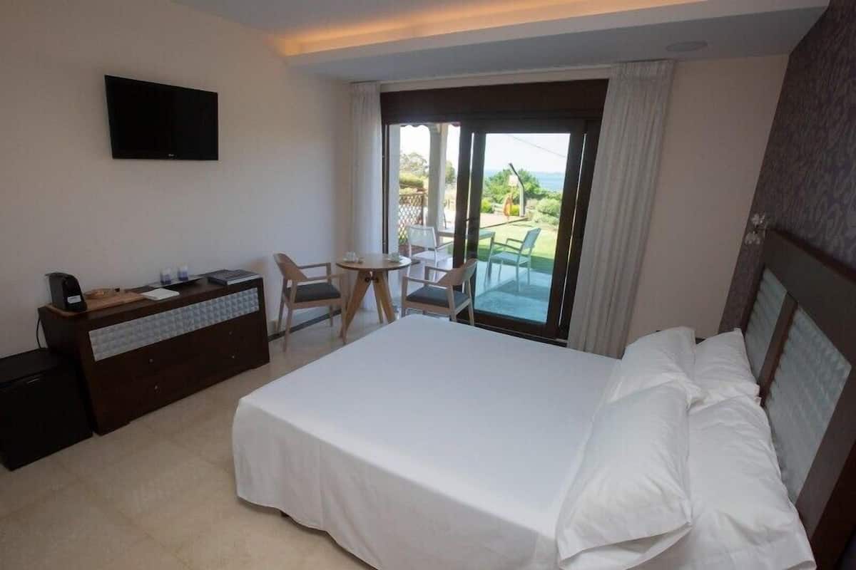 Une chambre d’hôtel avec un grand lit, un bureau avec un téléphone, une chaise, une petite table et un balcon avec vue.