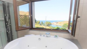 A bathroom with a large bathtub, a glass shower enclosure, and a window offering a view of a lake and hills. - A Ballenera de Caneliñas (Cee)
