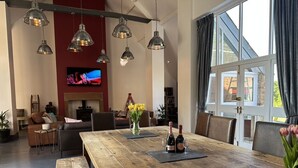 Un salon spacieux avec une table à manger en bois, des luminaires suspendus modernes, une cheminée et une grande fenêtre agrémentée de rideaux.
