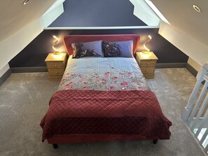 A bedroom with a bed, two bedside tables, a red headboard, and a skylight above.