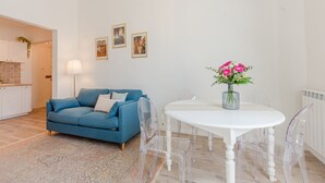 A modern living room with a blue sofa, a white dining table with clear chairs, and a vase of flowers. - Belvilla by OYO Maison (Fucecchio)