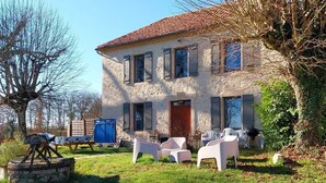 Ein zweistöckiges Haus mit rotem Ziegeldach, einer Haustür und einem kleinen Garten mit weißen Plastikstühlen.