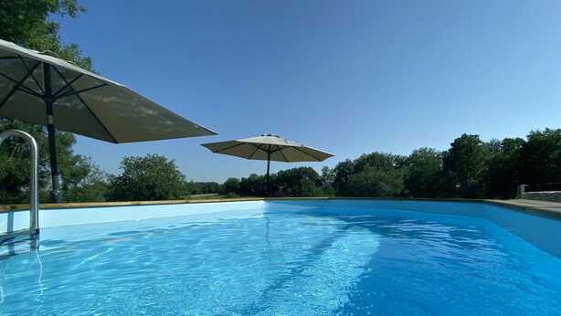 Ein klares, blaues Schwimmbecken mit zwei Sonnenschirmen, die Schatten spenden.
