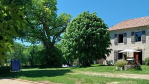 Ein Innenhof mit einem Bocciafeld, einem großen Baum und einem Haus mit Ziegeldach.