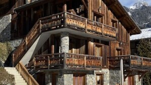 A wooden chalet with a stone foundation, a balcony, and a staircase leading to the entrance.