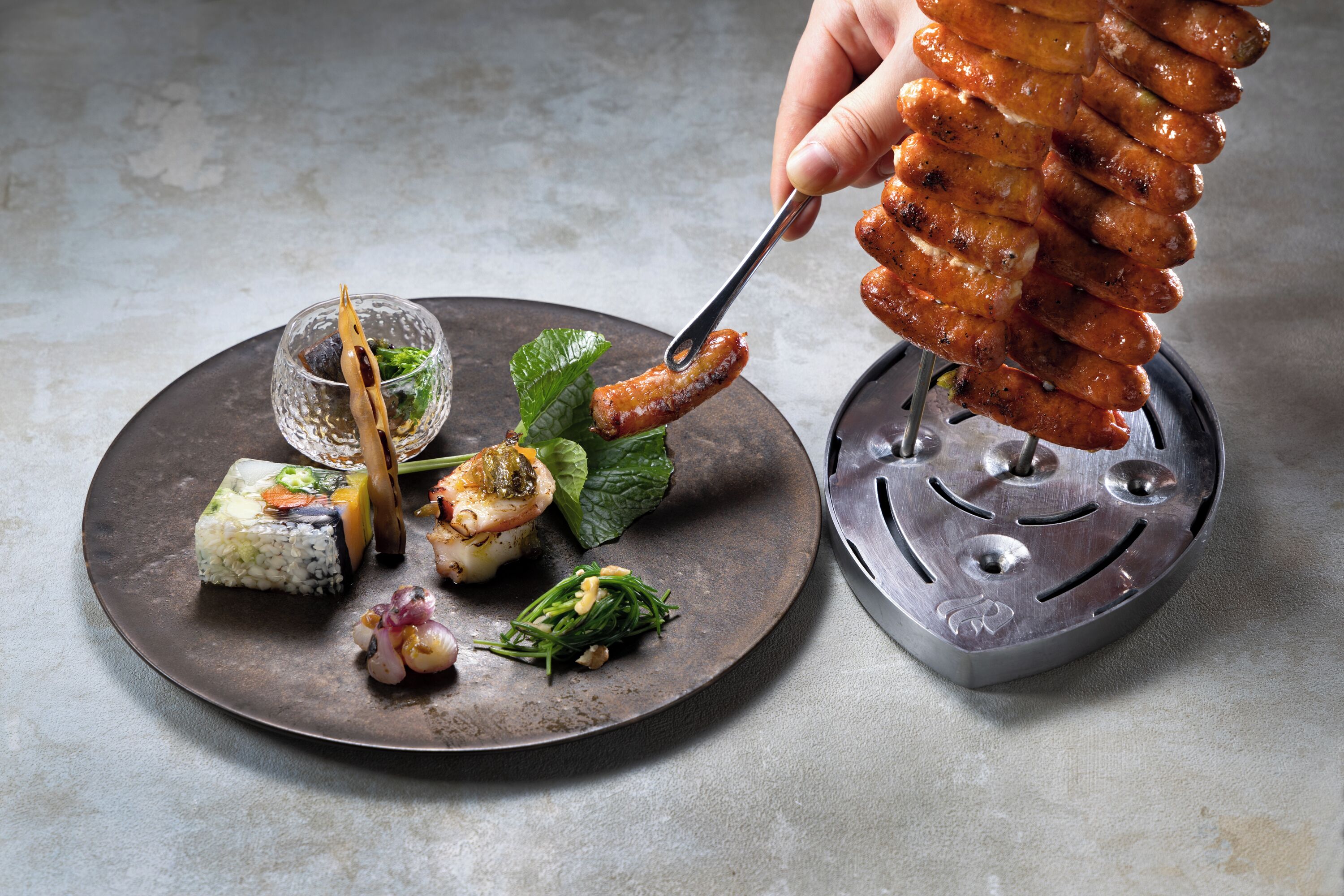 A plate with sushi, a skewer of grilled meat, and a small bowl of sauce.