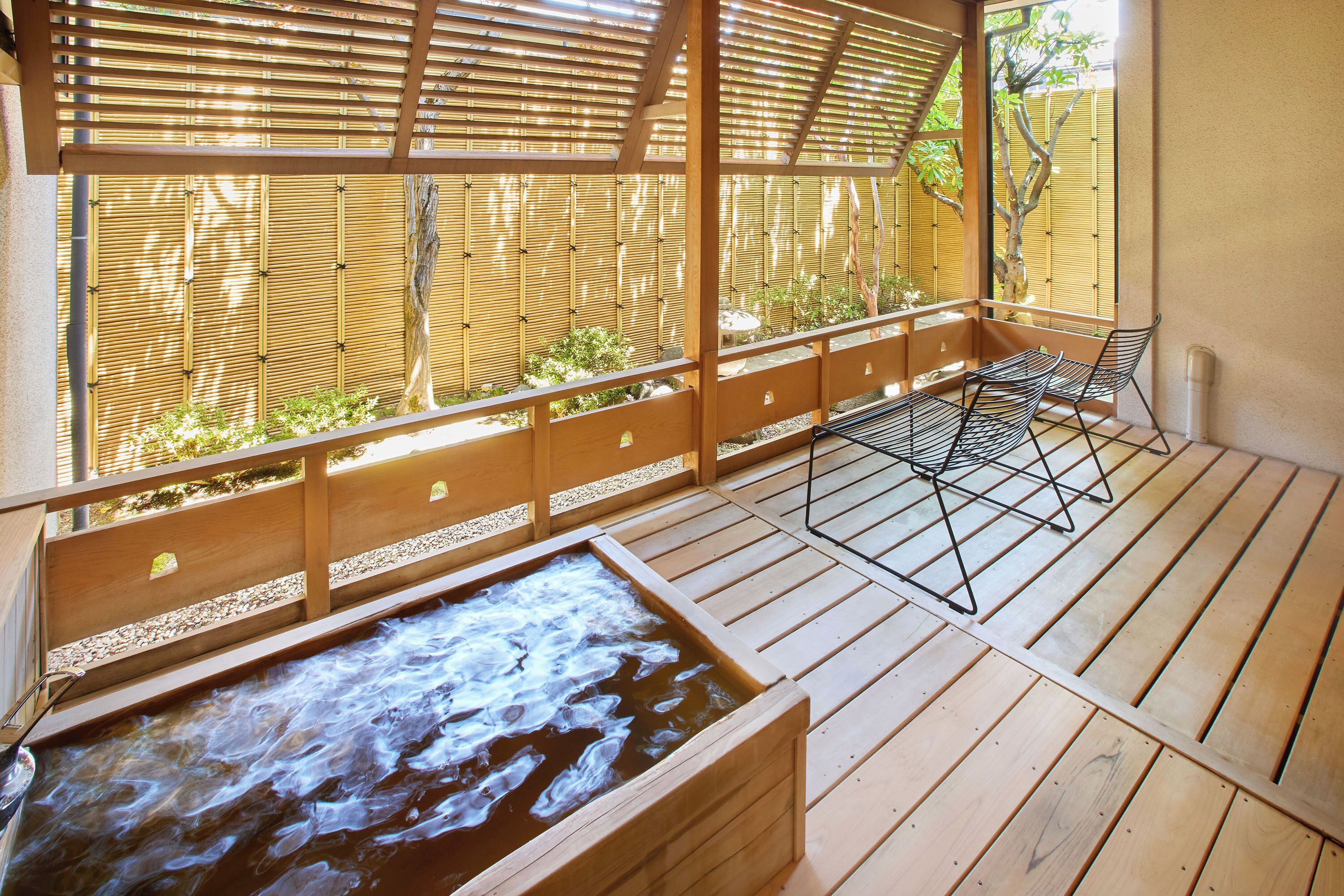 Terraza de madera con aguas termales, pantalla de bambú y una zona de estar.