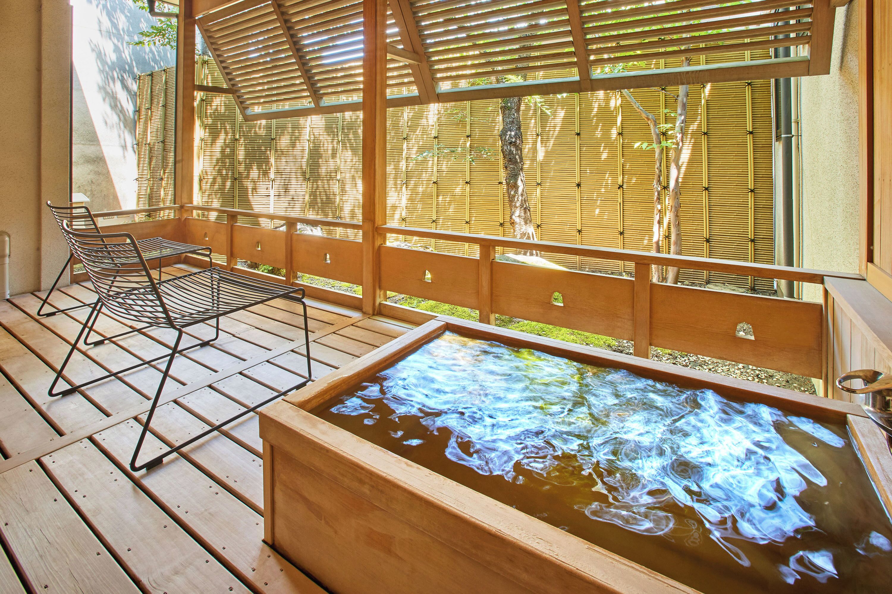Una terraza de madera con un jacuzzi, una silla metálica y una valla de bambú.