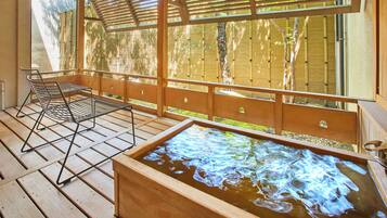 Una terraza de madera con un jacuzzi, una silla metálica y una valla de bambú.