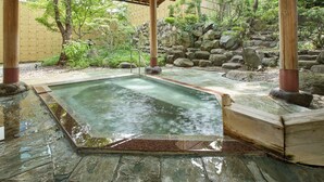 Een traditionele Japanse onsen met een stenen warmwaterbron, houten pilaren en een bamboe hek op de achtergrond.