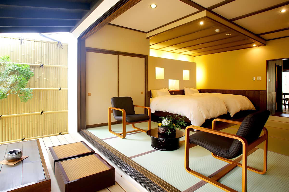 Ein traditionell japanisch gestaltetes Hotelzimmer mit Tatami-Böden, einem niedrigen Bett und einer Schiebetür zu einem Balkon mit Blick auf Bambus.