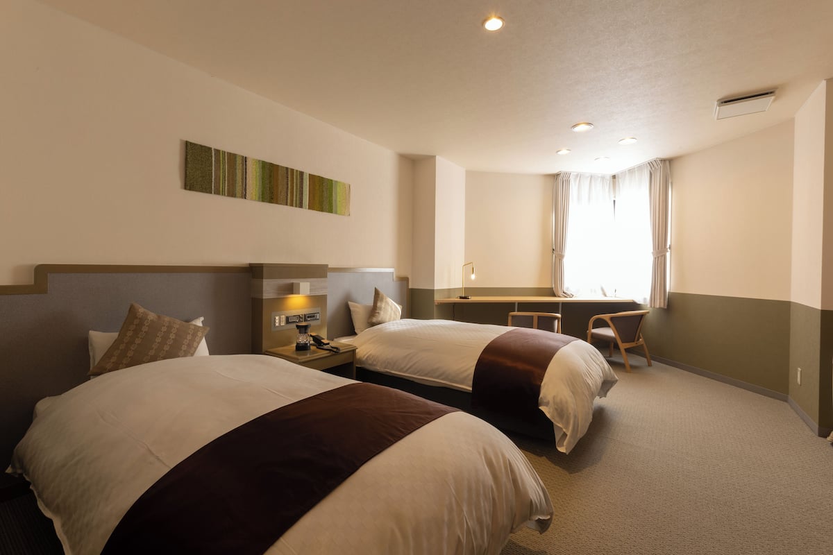 Ein Hotelzimmer mit zwei Betten, einem Schreibtisch und einem Stuhl.