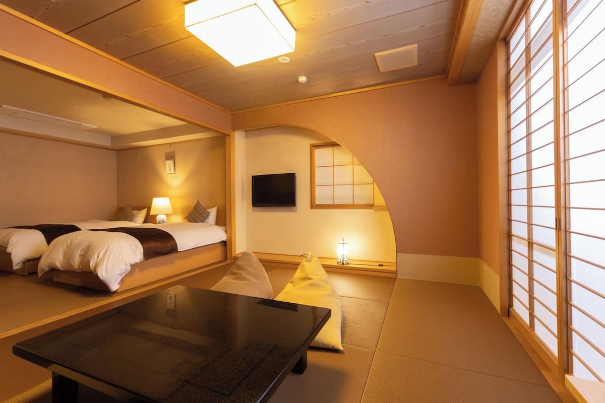 Ein Hotelzimmer mit zwei Betten, einem kleinen Tisch, einem Fernseher und einer traditionellen japanischen Schiebetür.