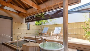 Een traditionele Japanse onsen met een houten terras, een warmwaterbron en twee lounge fauteuils.