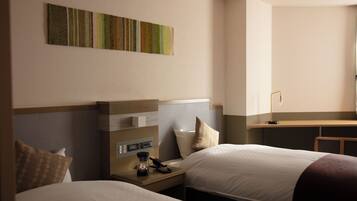 A hotel room with two beds, a desk, a lamp, and a wall-mounted artwork.