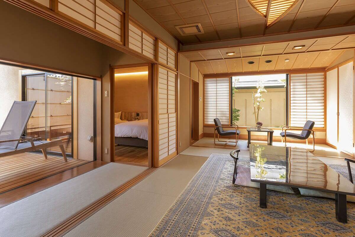 Ein traditioneller japanischer Raum mit Tatami-Böden, Schiebetüren, einem Bett, einem Esstisch und Blick ins Freie.