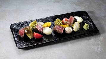 Un plato rectangular negro con diversos alimentos, incluyendo carne, verduras y posiblemente algunos condimentos.