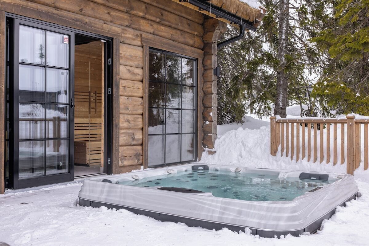 Een houten chalet met een jacuzzi in de sneeuw.