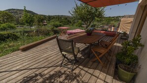 A wooden deck with a table and chairs, surrounded by potted plants and a red umbrella.