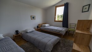 A bedroom with two single beds, a wooden nightstand, a small table, a chair, and a window with curtains.