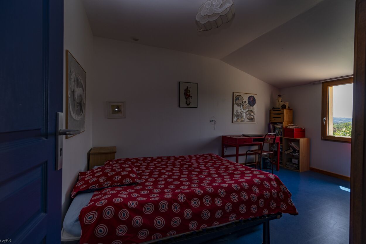A bedroom with a bed, a desk, and a chair. There is a window with a view of the outdoors.