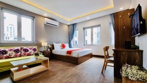 Une chambre d’hôtel moderne équipée d’un lit, d’un bureau, d’une télévision et de grandes fenêtres.