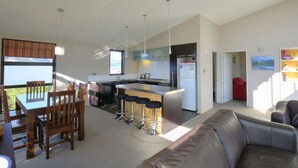 A modern kitchen with a central island, bar stools, and a dining area with a table and chairs. - Anderson Heights | Spacious Stay with lake views (Wānaka)