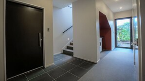 A modern hallway with a dark door, a staircase, and a glass door leading outside. - Anderson Heights | Spacious Stay with lake views (Wānaka)