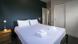 A neatly made bed with white linens and towels, a bedside lamp, and a dark-colored wall. - Anderson Heights | Spacious Stay with lake views (Wānaka)