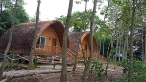 Dos chozas con techo de paja y barandillas de madera, rodeadas de árboles.