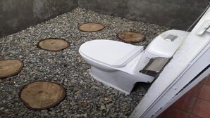 Baño pequeño y cerrado con un inodoro blanco, un cesto de basura y cuatro escalones de madera que conducen a un nivel superior.