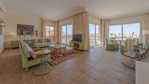 Ein geräumiges Wohnzimmer mit großem Fernseher, grünen Sofas und Blick auf den Strand.