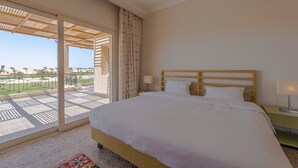 Ein Hotelzimmer mit einem großen Bett, einem Balkon mit Blick auf Palmen und einer Holzbalkendecke.