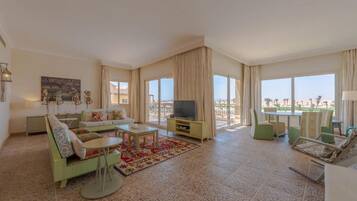 A spacious living room with a sofa, coffee table, and TV, large windows with curtains, and a view of the outdoors.