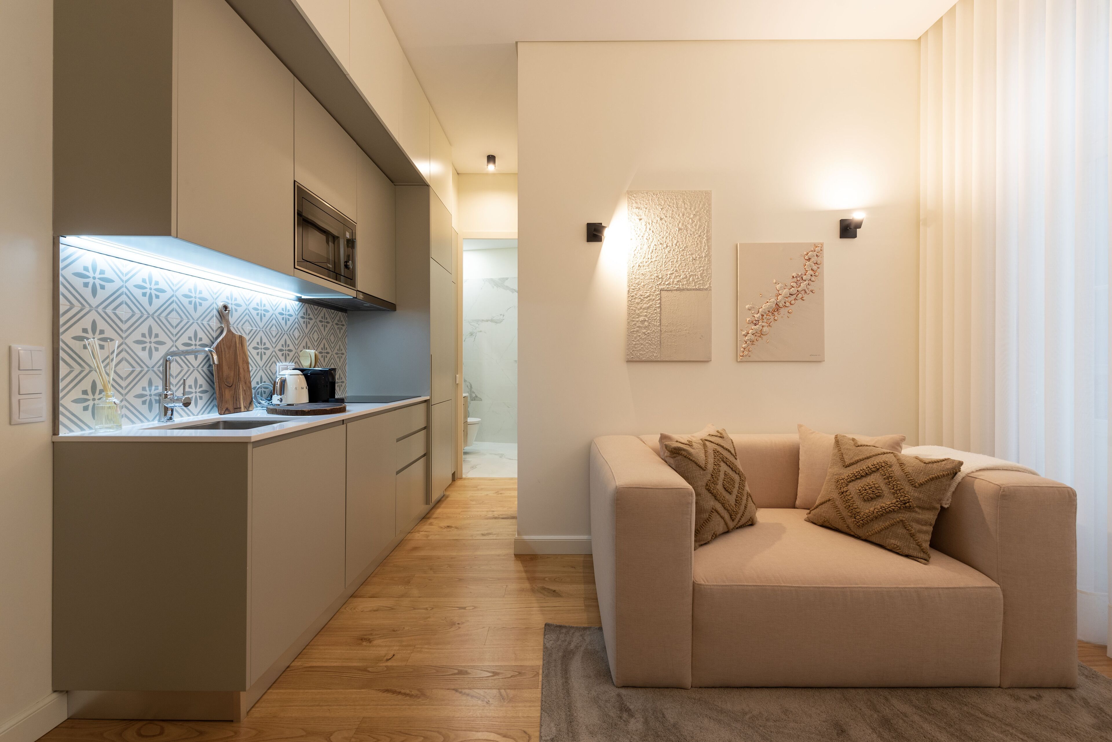 A modern kitchen with a built-in oven, a wooden cutting board, and a kettle on the counter.